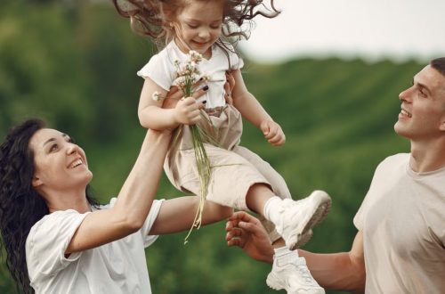 Happy family enjoying playful outdoor moment, lifting child in summer day.