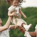 Happy family enjoying playful outdoor moment, lifting child in summer day.